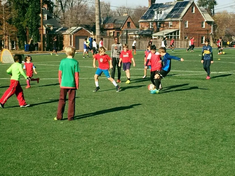 2015: Children in red, green and other shirts chase the ball in a game.