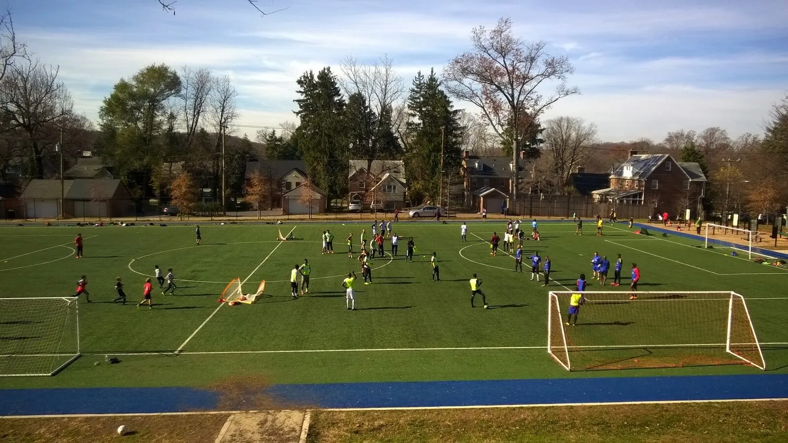 2015: A wide view of a turf field with many players in several games under a blue sky.