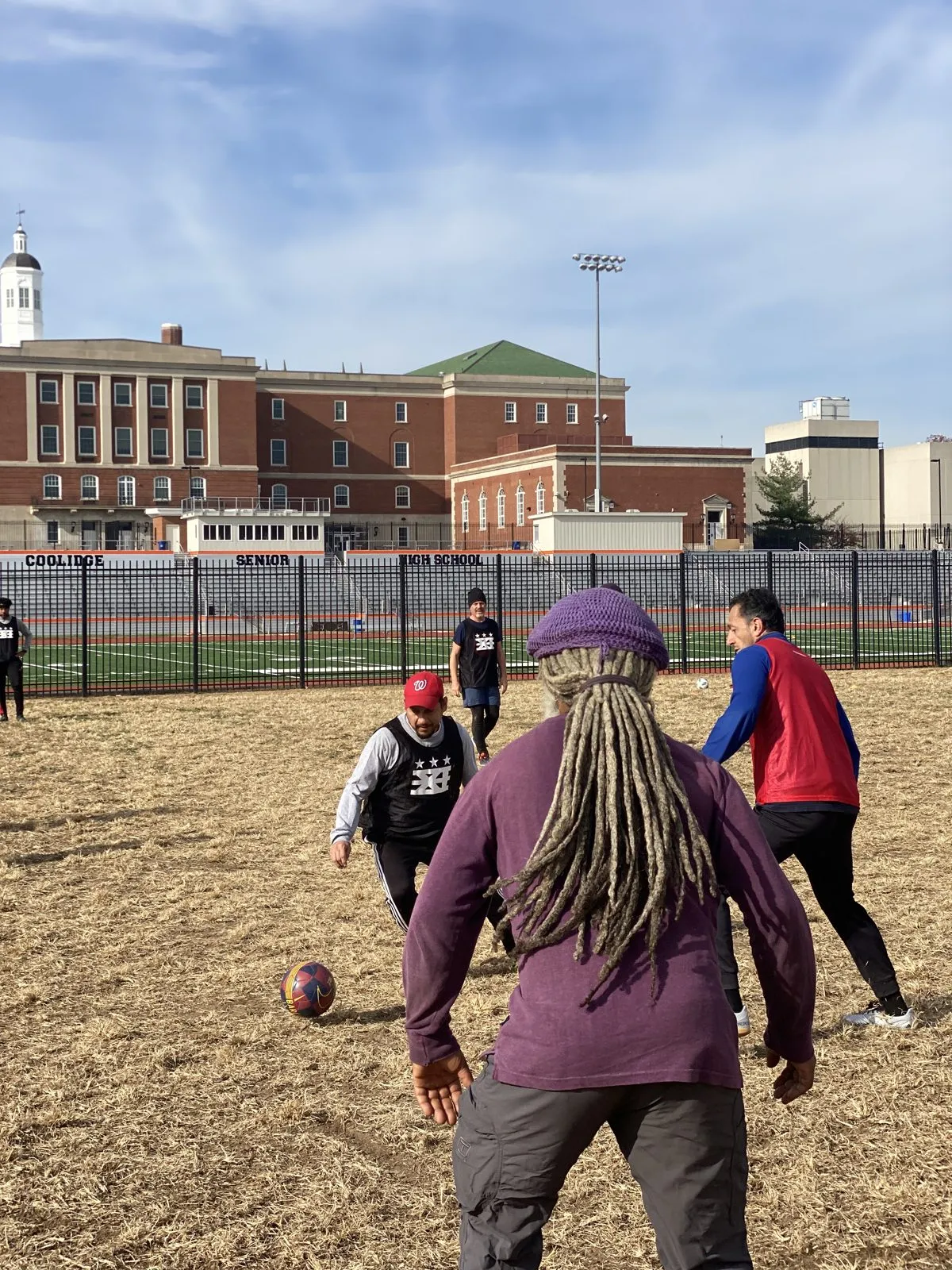 2021: A player in a purple hat and a goalkeeper in a red bib stand on a dry grass field during pick-up.