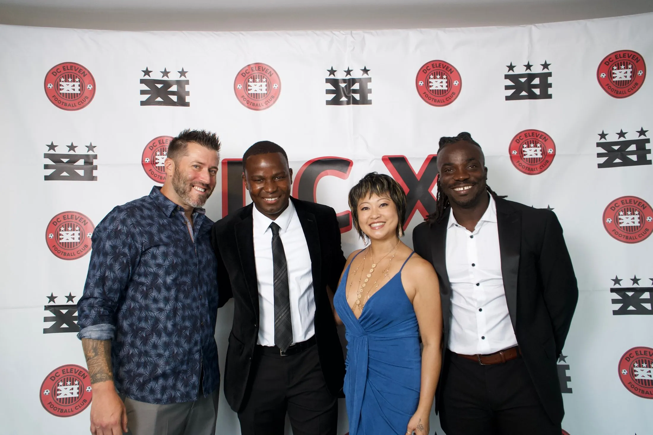 Four gala guests, two women and two men, pose together in front of a DC XI backdrop.