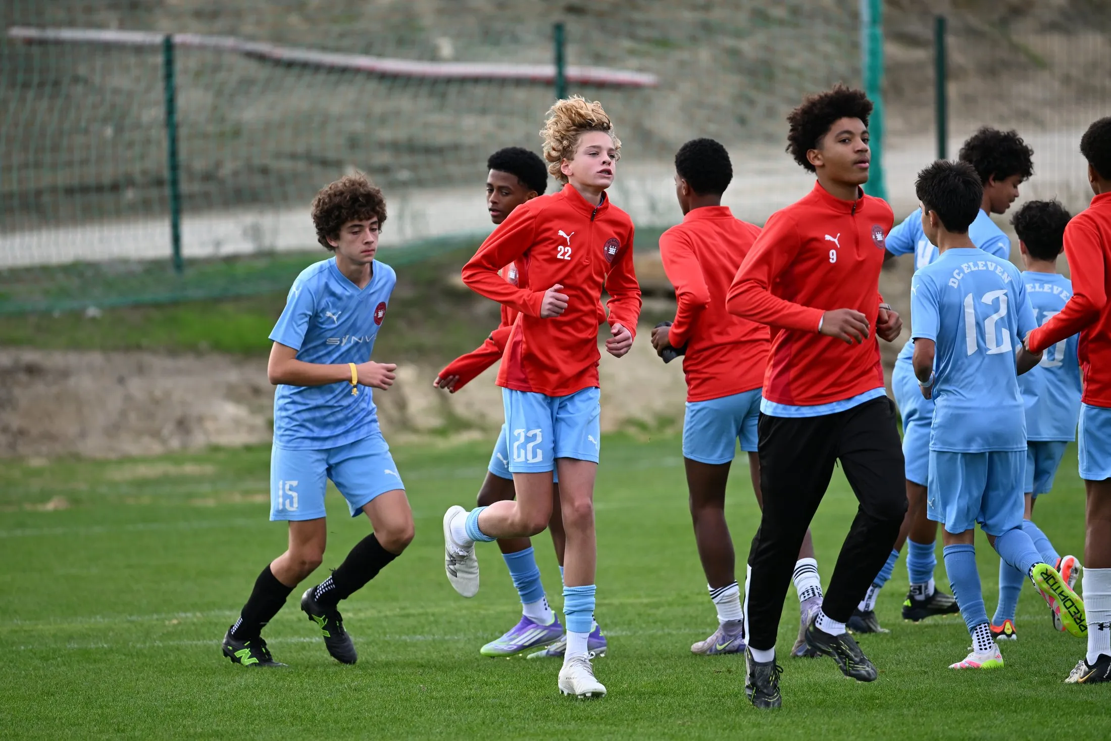 Teenage players in light blue and red tops warm up together before training.