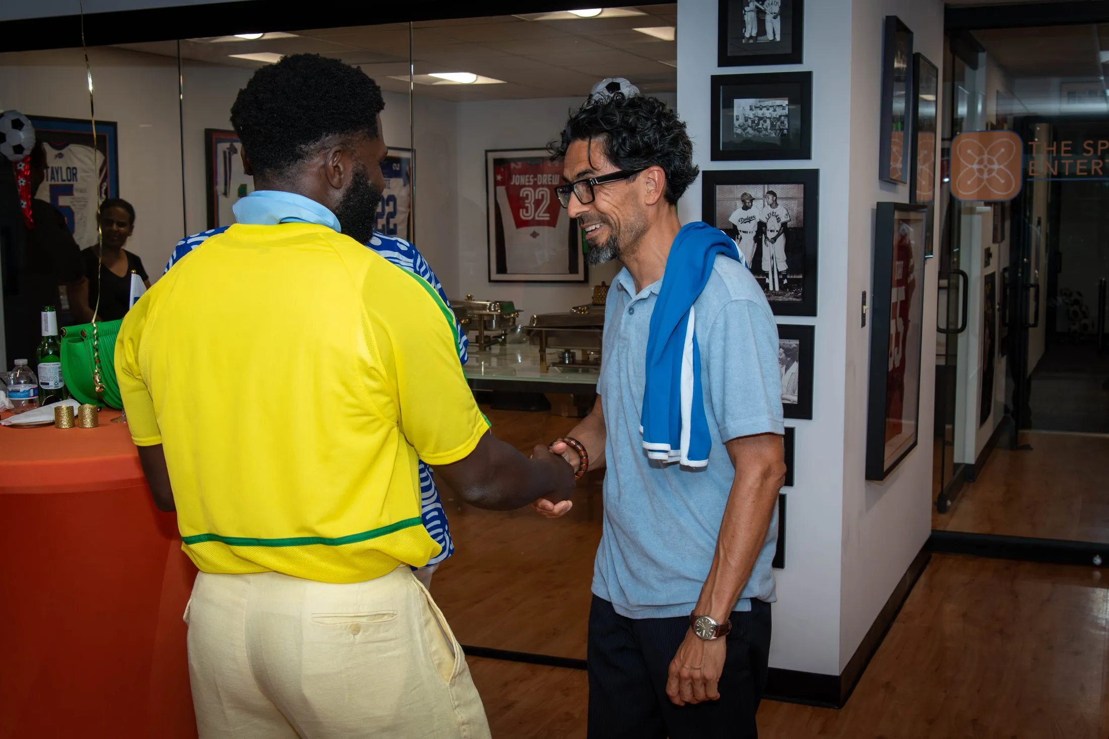 Two gala guests shake hands, one wearing a yellow football jersey.