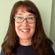 Maureen Valencia, smiling, with glasses and long brown hair, wearing a navy DC Eleven shirt