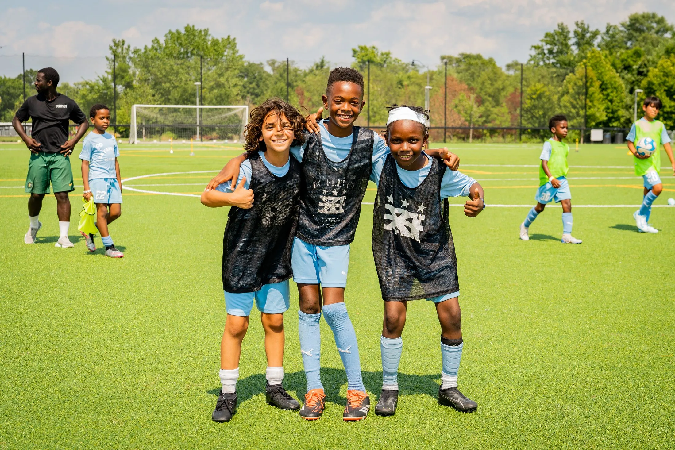 Three smiling campers stand arm in arm on a turf field.