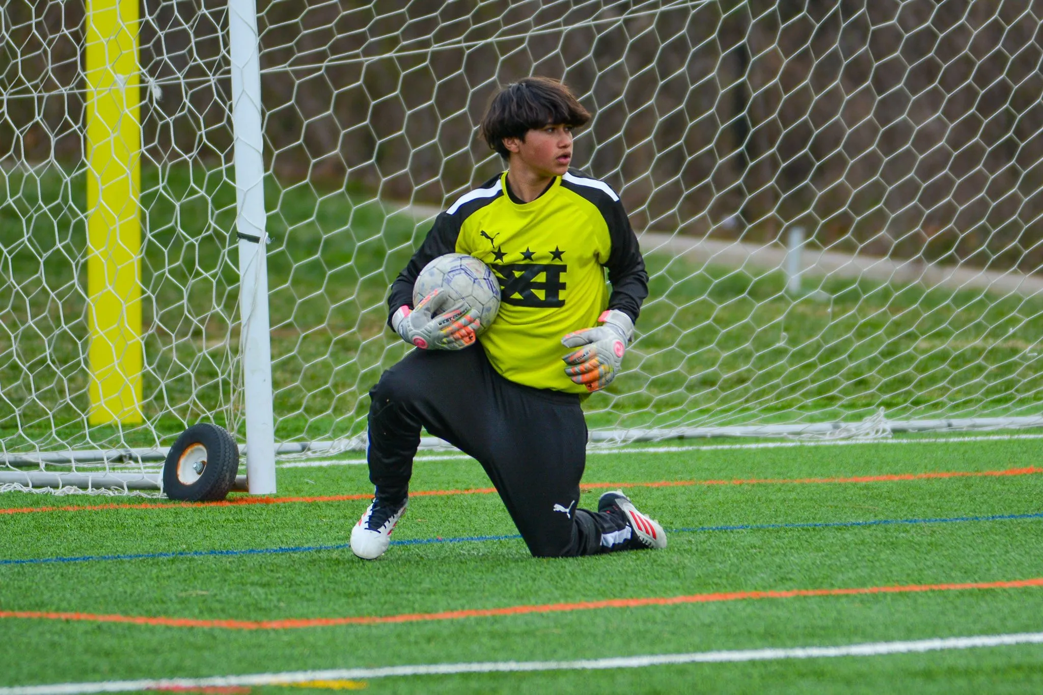 A goalkeeper in a yellow jersey kneels in goal holding the ball.